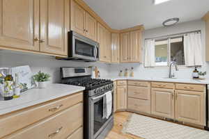 Kitchen with appliances with stainless steel finishes, light brown cabinets, light countertops, and light wood finished floors