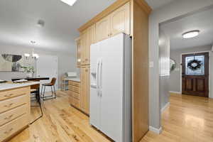 Kitchen with white refrigerator with ice dispenser, light brown cabinets, light countertops, and light wood-style floors