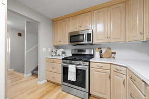 Kitchen with light brown cabinets, stainless steel appliances, light wood-style floors, and light countertops