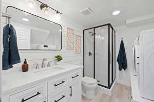 Bathroom with washer / dryer, vanity, a stall shower, and wood finished floors