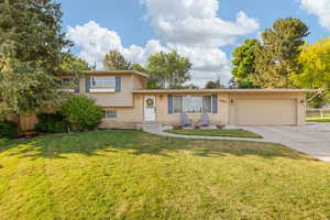 Split level home with an attached garage, concrete driveway, brick siding, and a front yard