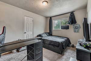 Carpeted bedroom featuring a textured ceiling, cooling unit, and a textured wall