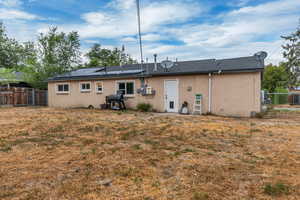 Rear view of house featuring stucco siding, a fenced backyard, roof mounted solar panels, and a shingled roof