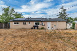 Rear view of house with stucco siding, a fenced backyard, and solar panels