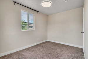 Carpeted empty room featuring a textured ceiling and baseboards
