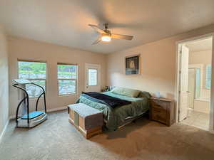 Carpeted bedroom with multiple windows, ensuite bathroom, a ceiling fan, and a textured ceiling