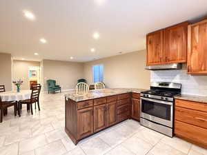 Kitchen featuring stainless steel range with gas cooktop, under cabinet range hood, a peninsula, recessed lighting, and granite countertops