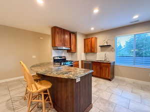 Kitchen featuring stainless steel appliances, under cabinet range hood, brown cabinets, tasteful backsplash, and a peninsula