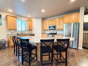 Kitchen with appliances with stainless steel finishes, a kitchen island, dark wood-type flooring, a breakfast bar, and light stone counters