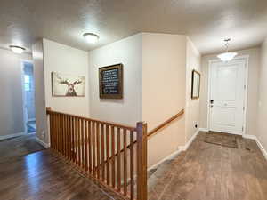 Hallway with wood-type flooring, an upstairs landing, and a textured ceiling