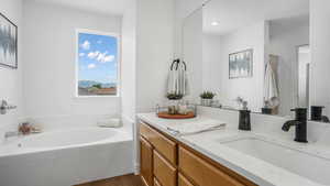 Full bath with double vanity, a garden tub, and wood finished floors