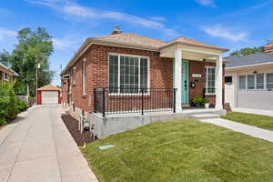 View of front of house with a detached garage, brick siding, a front lawn, an outdoor structure, and a porch