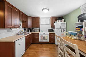 Kitchen featuring white appliances, backsplash, light countertops, and wood finished floors
