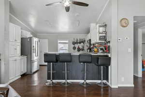 Kitchen with appliances with stainless steel finishes, a peninsula, a ceiling fan, white cabinetry, and crown molding