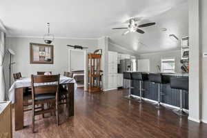 Dining space featuring ceiling fan, dark wood-style flooring, lofted ceiling, and ornamental molding