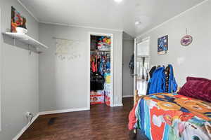 Bedroom with wood finished floors, ornamental molding, and a closet