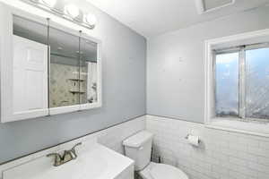 Full bathroom featuring tile walls, a textured ceiling, wainscoting, vanity, and a shower with shower curtain