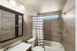 Bathroom with shower / bath combo, vanity, and tile walls