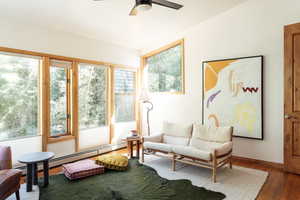 Living area featuring healthy amount of natural light, wood-type flooring, ceiling fan, and a baseboard heating unit