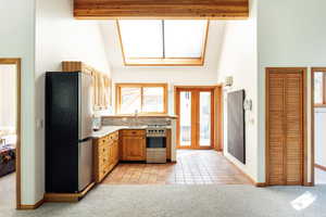 Kitchen featuring appliances with stainless steel finishes, high vaulted ceiling, light colored carpet, light countertops, and backsplash