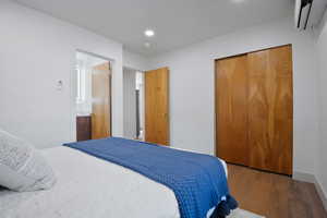 Bedroom featuring an AC wall unit, wood finished floors, a closet, and recessed lighting