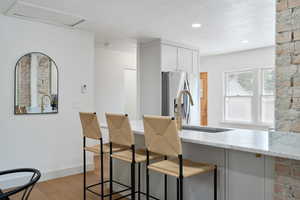 Kitchen featuring light wood-style flooring, stainless steel refrigerator with ice dispenser, light stone counters, a breakfast bar, and a textured ceiling