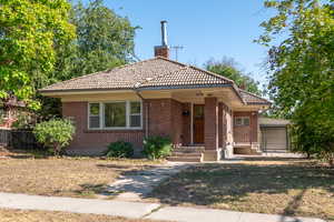Bungalow-style home featuring brick siding, a chimney, a tile roof, and a garage