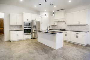 Gourmet kitchen with stainless steel appliances, custom range hood, black quartz countertops, tasteful backsplash, white cabinets, and vaulted ceiling.