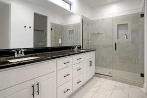 Primary bathroom featuring double vanity, euro-style shower, black quartz, and white cabinets.