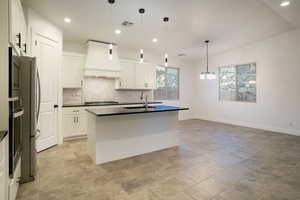 Gourmet kitchen with stainless steel appliances, custom range hood, black quartz countertops, tasteful backsplash, white cabinets, and vaulted ceiling.