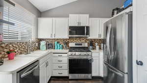 Kitchen featuring appliances with stainless steel finishes, lofted ceiling, backsplash, white cabinets, and light countertops