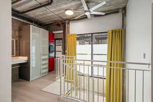 Hall with stacked washer and clothes dryer, wood finished floors, and an upstairs landing