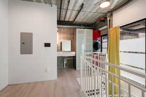Hallway with electric panel, wood finished floors, and stacked washer and clothes dryer