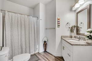 Full bath with toilet, vanity, wood finished floors, baseboards, and curtained shower
