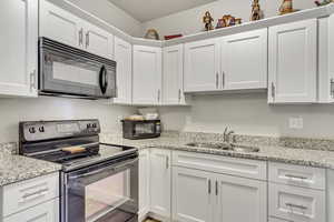 Kitchen with black appliances, a sink, white cabinetry, and light stone counters