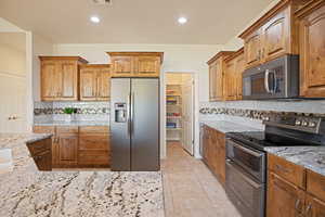 Kitchen with stainless steel appliances, light stone countertops, tasteful backsplash, brown cabinetry, and recessed lighting