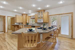 Kitchen with microwave, a breakfast bar, stainless steel dishwasher, light wood finished floors, and glass insert cabinets