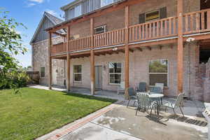 Back of property with brick siding, a patio, board and batten siding, and a balcony