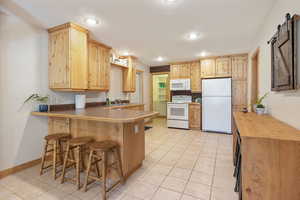 Kitchen with a peninsula, light tile patterned floors, a kitchen breakfast bar, and a barn door