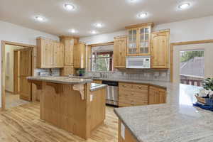 Kitchen featuring white microwave, dishwasher, a kitchen breakfast bar, light wood floors, and glass insert cabinets