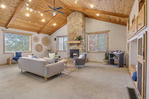 Carpeted living room with a wooden ceiling with exposed beams, a fireplace, a ceiling fan, high vaulted ceiling, and track lighting