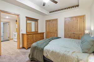 Bedroom featuring light tile patterned floors, light carpet, a ceiling fan, and connected bathroom