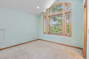 Carpeted spare room with baseboards and lofted ceiling