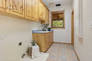 Laundry area with hookup for an electric and gas dryer, cabinet space, and light tile floors