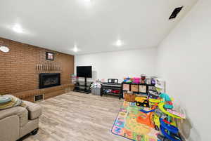 Rec room with a fireplace, wood finished floors, recessed lighting, and brick wall