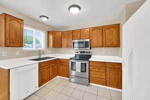 Kitchen with appliances with stainless steel finishes, brown cabinets, light countertops, and light tile patterned floors