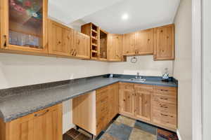 Kitchen featuring dark countertops, dark stone finish floors, glass insert cabinets, and light brown cabinets