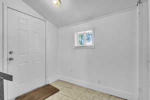 Backdoor entrance with light tile patterned flooring and lofted ceiling