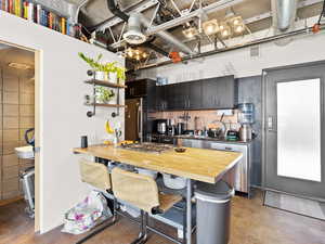 Kitchen with appliances with stainless steel finishes, finished concrete flooring, butcher block counters, and a breakfast bar