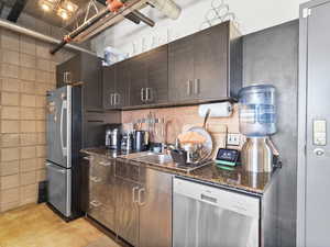 Kitchen with appliances with stainless steel finishes, dark stone counters, decorative backsplash, concrete flooring, and dark brown cabinetry